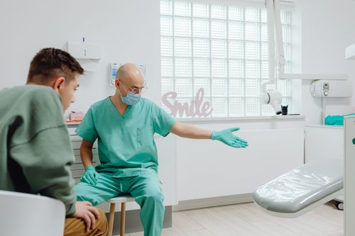 Free A dentist in green scrubs talks to a patient in a bright, modern dental clinic. Stock Photo