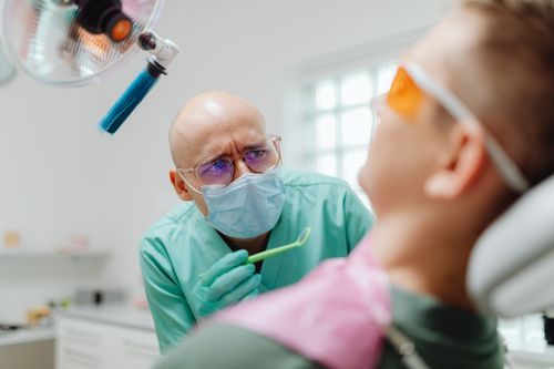 Free A bald dentist wearing eyeglasses examines a patient in a modern dental clinic. Stock Photo