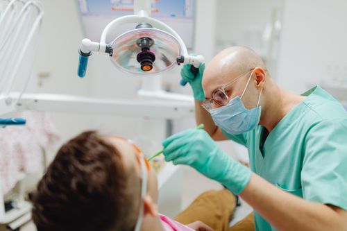 Free A dentist in green scrubs treating a patient under dental light in a clinic. Stock Photo