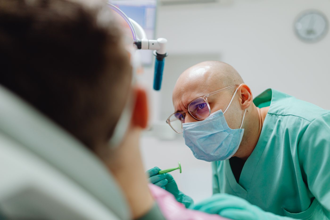 Masked dentist examining a seated patient in a bright modern dental office at Aurora Dental Studio