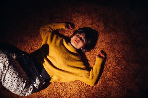 Free Woman posing on an orange carpet wearing a yellow sweater, creating a warm and artistic ambiance. Stock Photo