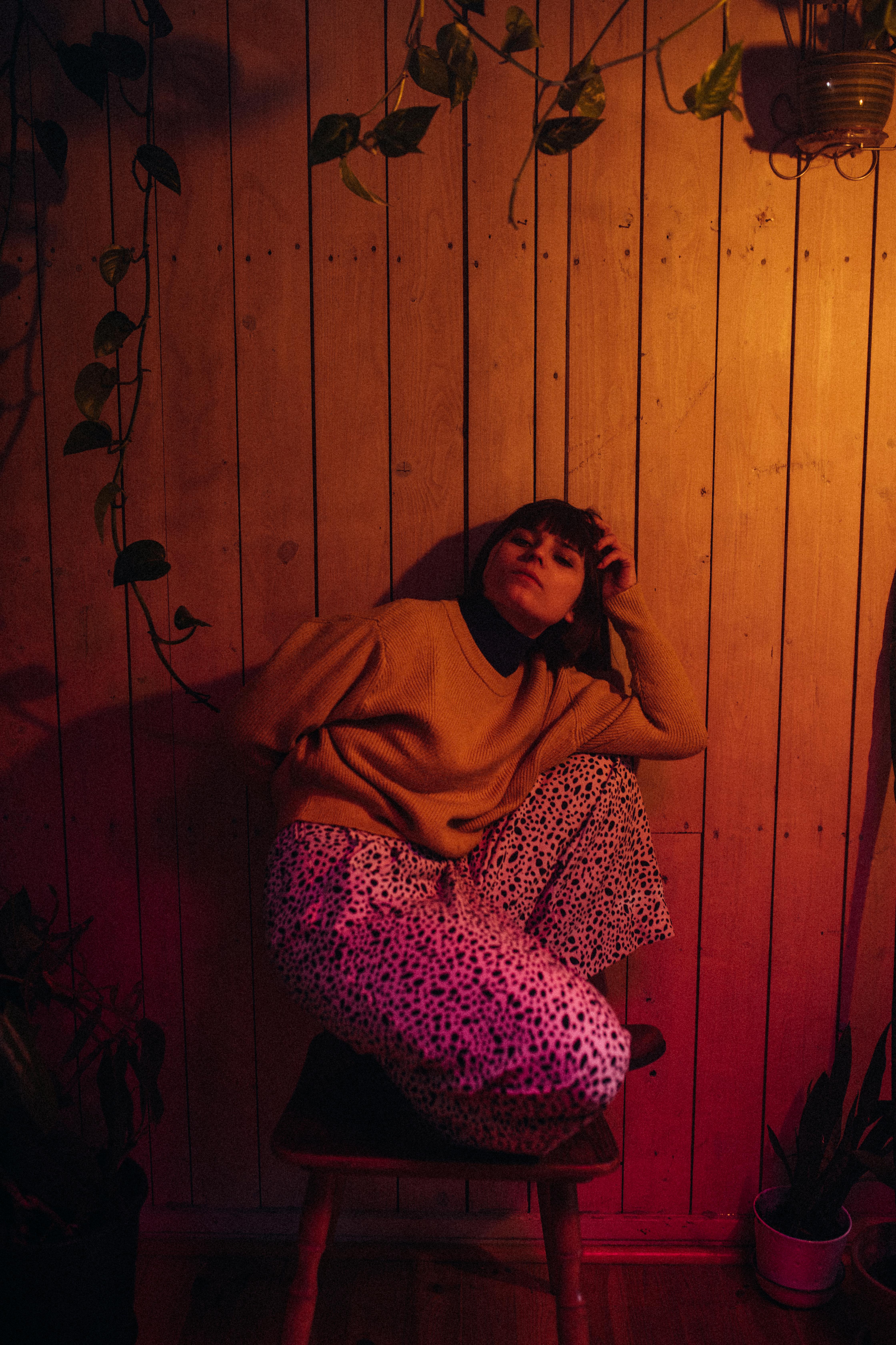 Trendy woman in cozy indoor environment with warm lighting, wearing stylish outfit.