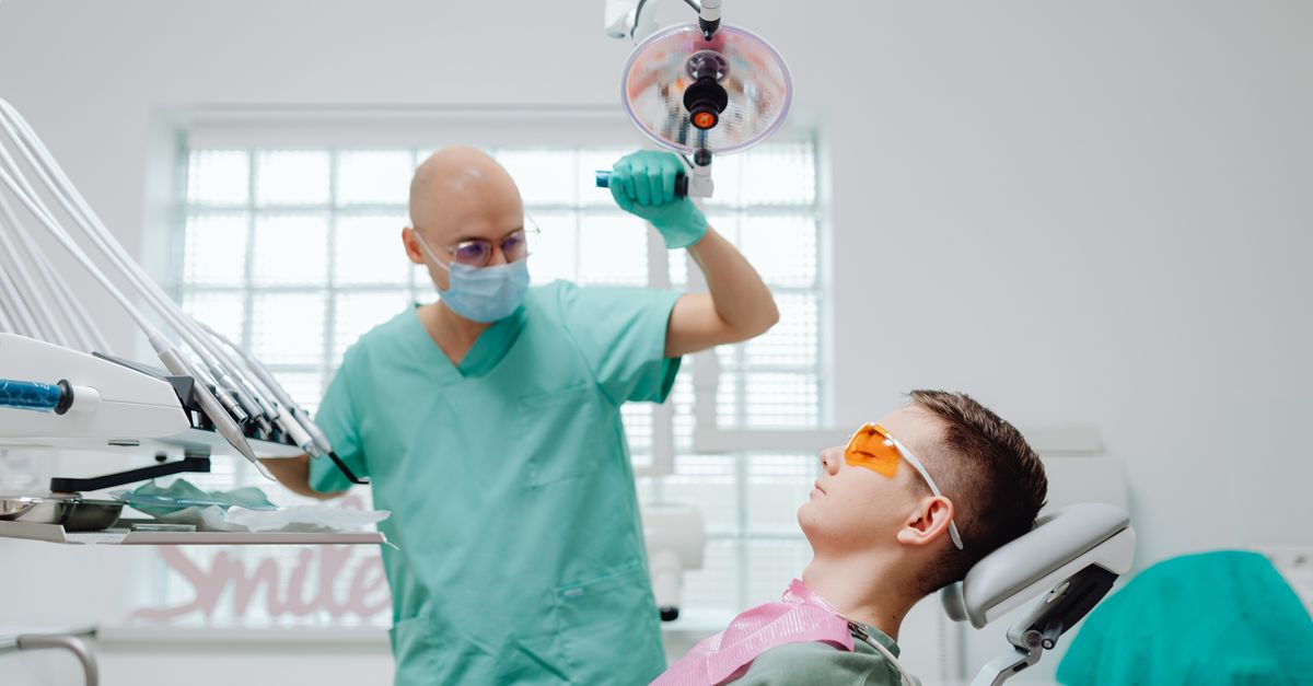 Un dentiste avec un masque chirurgical effectuant un examen sur un patient dans une clinique dentaire moderne.