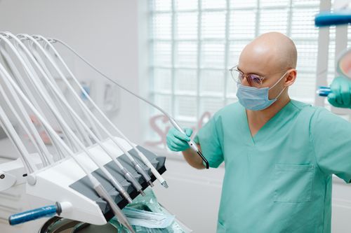 Free Dentist wearing mask and scrubs using dental instruments in a sterile clinic. Stock Photo