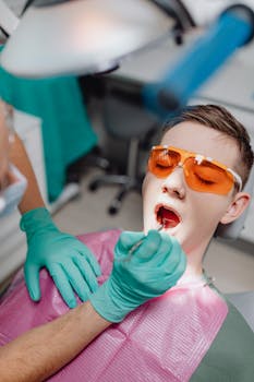 Close-up of a dentist performing a dental checkup on a young patient wearing protective glasses.