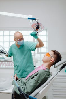Dentist in scrubs performing a dental checkup on a young male patient in a clinic.