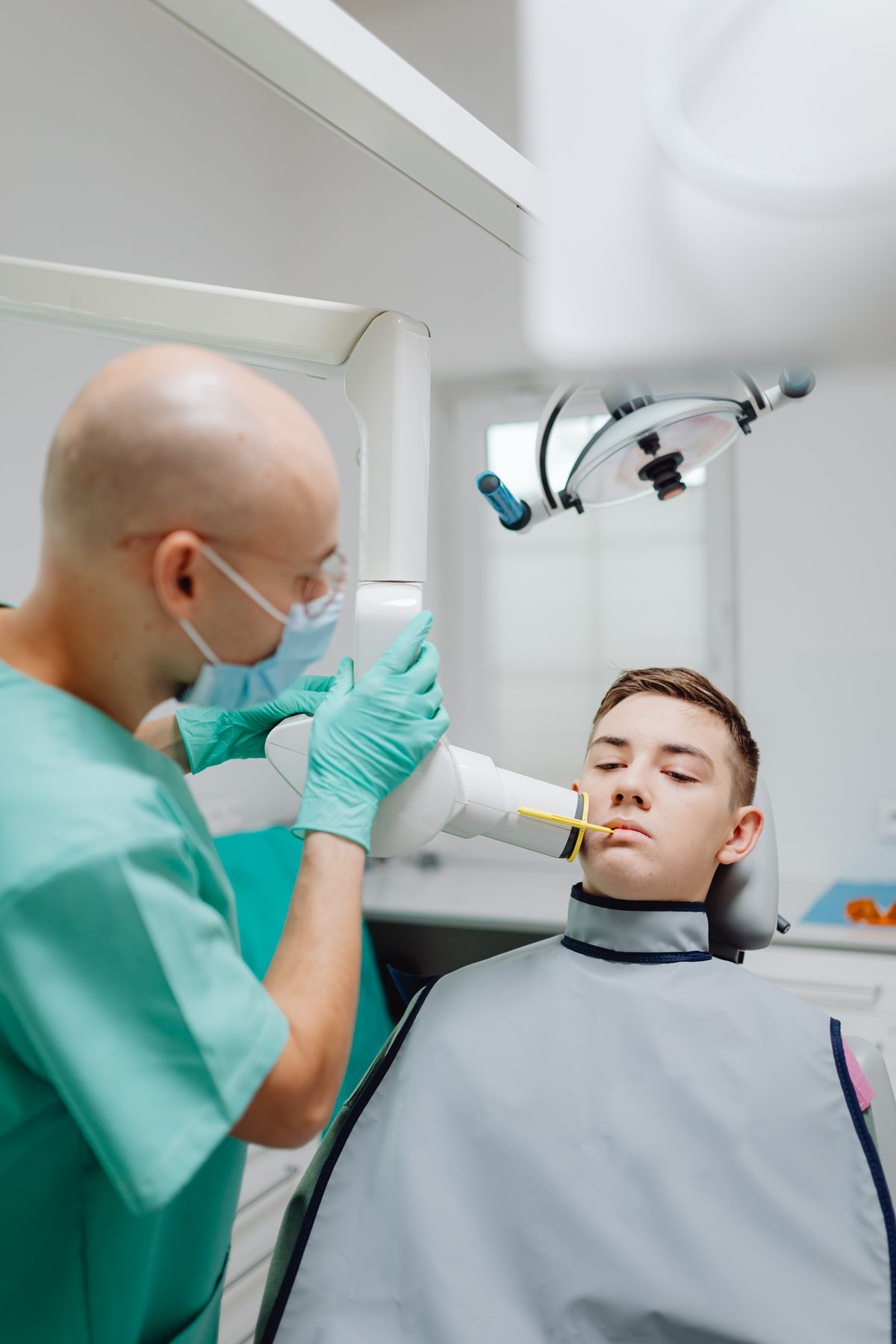 Odontólogo colocando el tubo de rayos X para tomar una radiografía intraoral a un paciente con delantal plomado