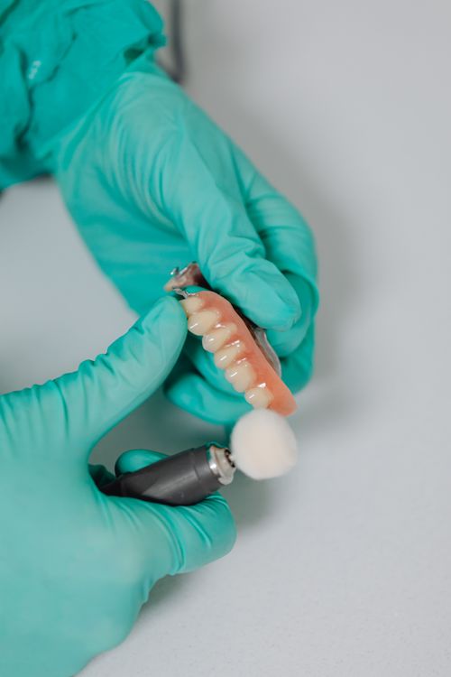 Free Dentist polishing dentures with rotary tool wearing green gloves in clinic. Stock Photo