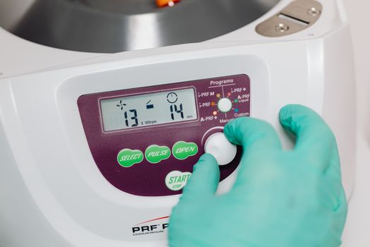 A gloved hand adjusts a control knob on a medical centrifuge device in a clinical setting.
