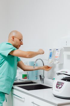 Doctor in medical attire washing hands in a sterile lab environment, emphasizing hygiene and disinfection.