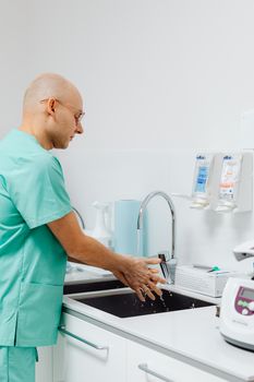 A doctor in scrubs washes hands at a medical facility sink, promoting hygiene and healthcare practices.