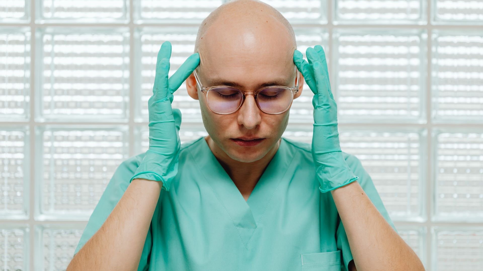 modafinil for surgeons: Is This Smart Drug the Answer to Surgical Fatigue? A surgeon in green scrubs appears stressed, holding their head with gloved hands indoors — modafinil for surgeons