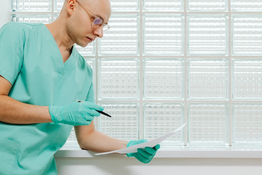 A healthcare worker in scrubs and gloves examines a document with focus.