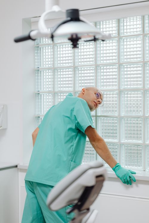 Free A dentist in green scrubs adjusting a lamp in a modern dental office with glass-block walls. Stock Photo