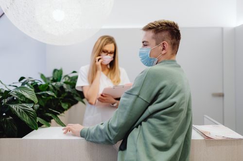 Free A patient and receptionist in a clinic wearing face masks, ensuring health safety. Stock Photo