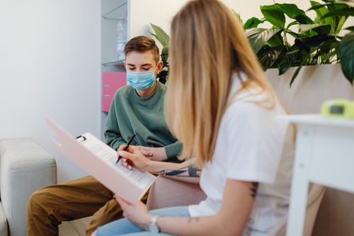 Free Teenage boy wearing a face mask during a consultation indoors, discussing with a female professional. Stock Photo