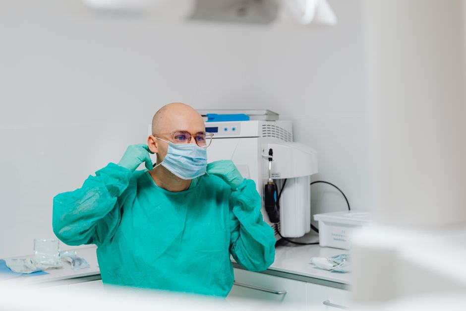 Bald medical practitioner in PPE adjusting face mask in clinic setting.