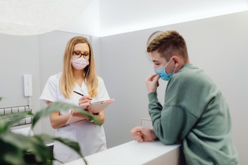 Free A healthcare worker consults a patient at a clinic reception, both wearing face masks. Stock Photo