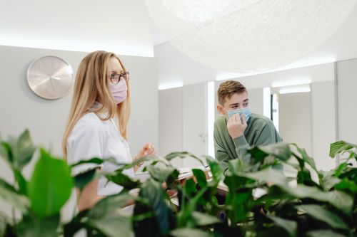 Free Man and woman wearing face masks in a clinic, discussing at a counter indoors. Stock Photo