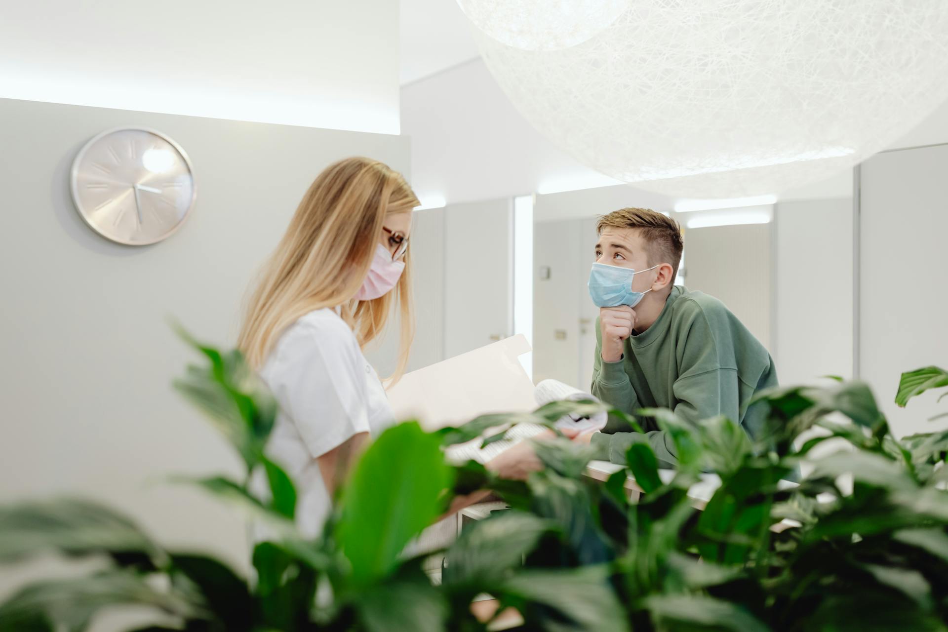 Masked individuals interacting at a modern clinic reception, focusing on safe communication.