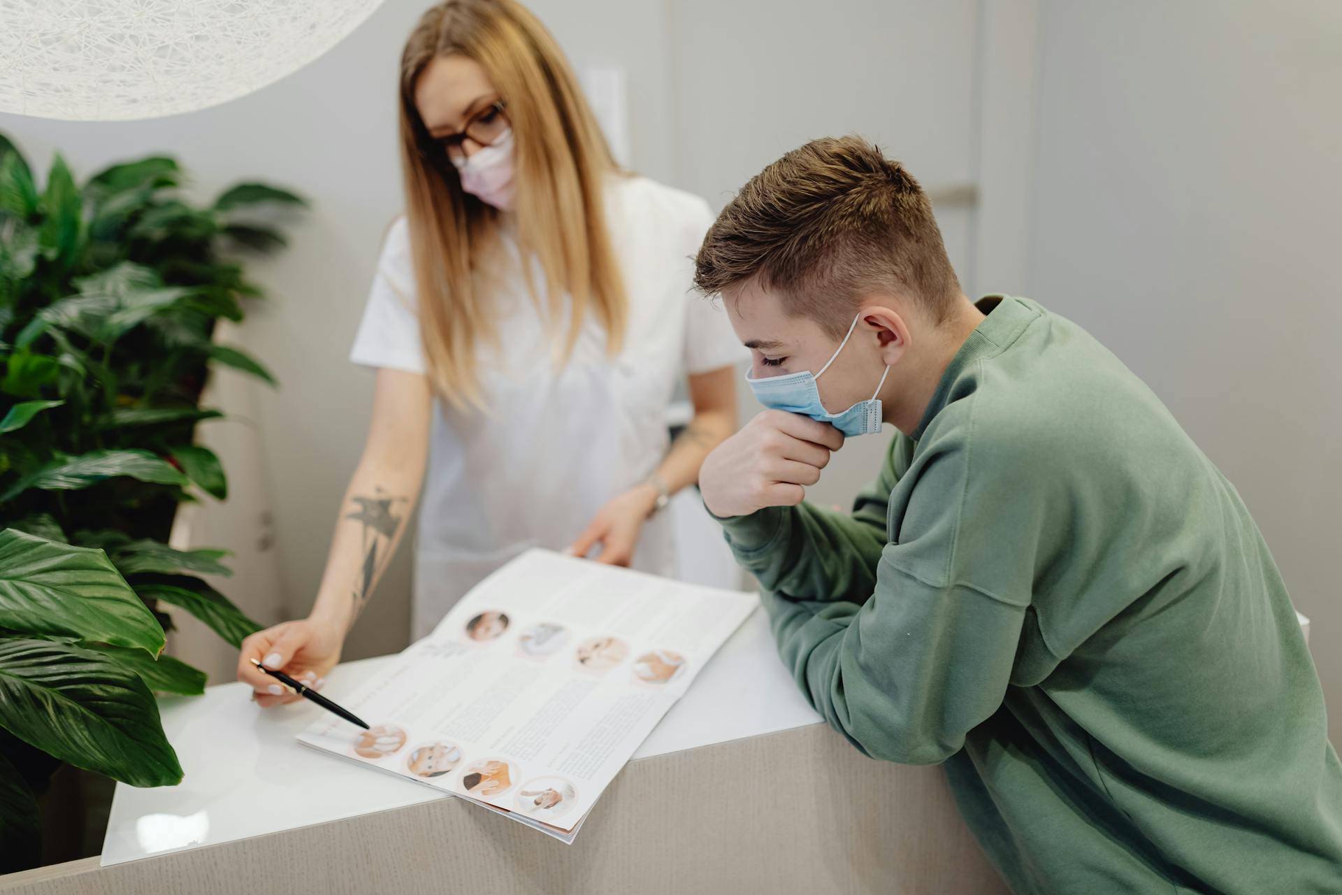 A healthcare professional and young man engaged in a consultation at a clinic, both wearing face masks for safety.