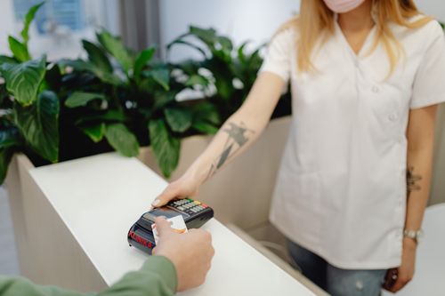Free Tattooed staff member assists credit card payment in a clinic setting. Stock Photo