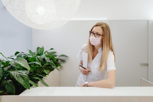 Free A female healthcare worker in a clinic wearing a face mask, standing at the reception desk. Stock Photo