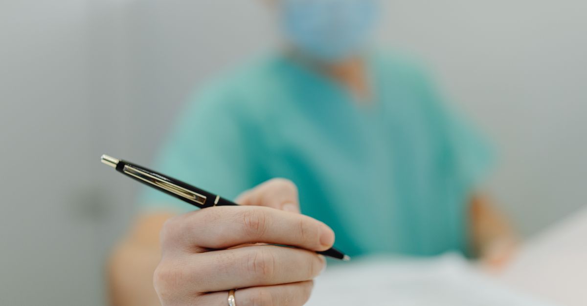 Close-up of a medical professional in scrubs writing with a pen, showing focus on hand and pen.
