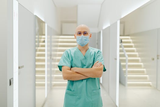 Healthcare worker in scrub suit stands confidently with arms crossed indoors.