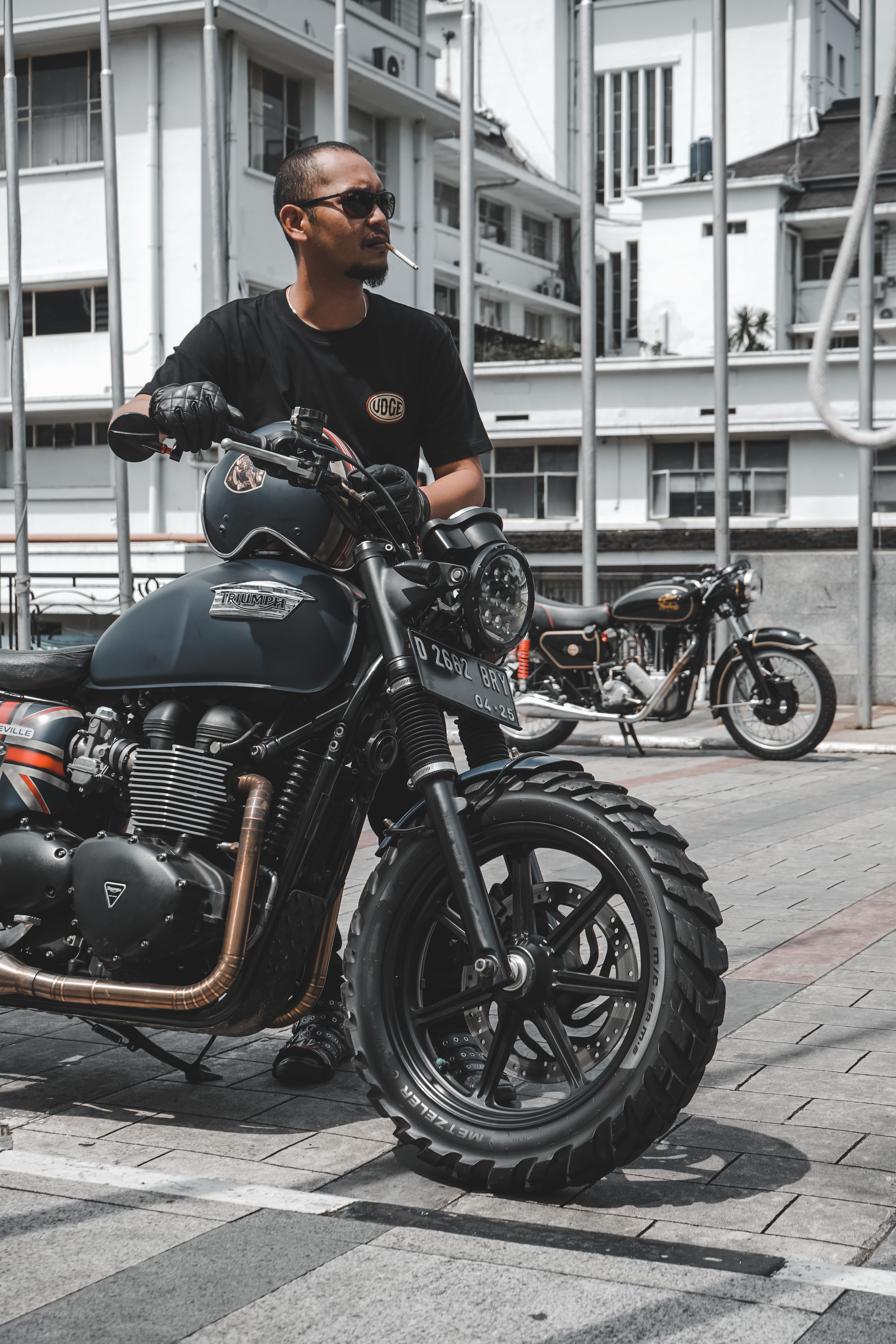A confident man in sunglasses standing beside a classic motorcycle on an urban street.