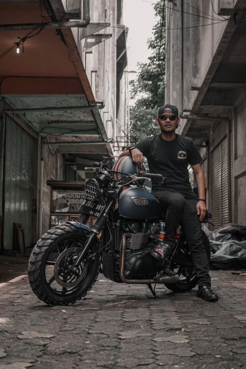 Free A biker confidently poses with a custom motorcycle in an urban alleyway setting. Stock Photo