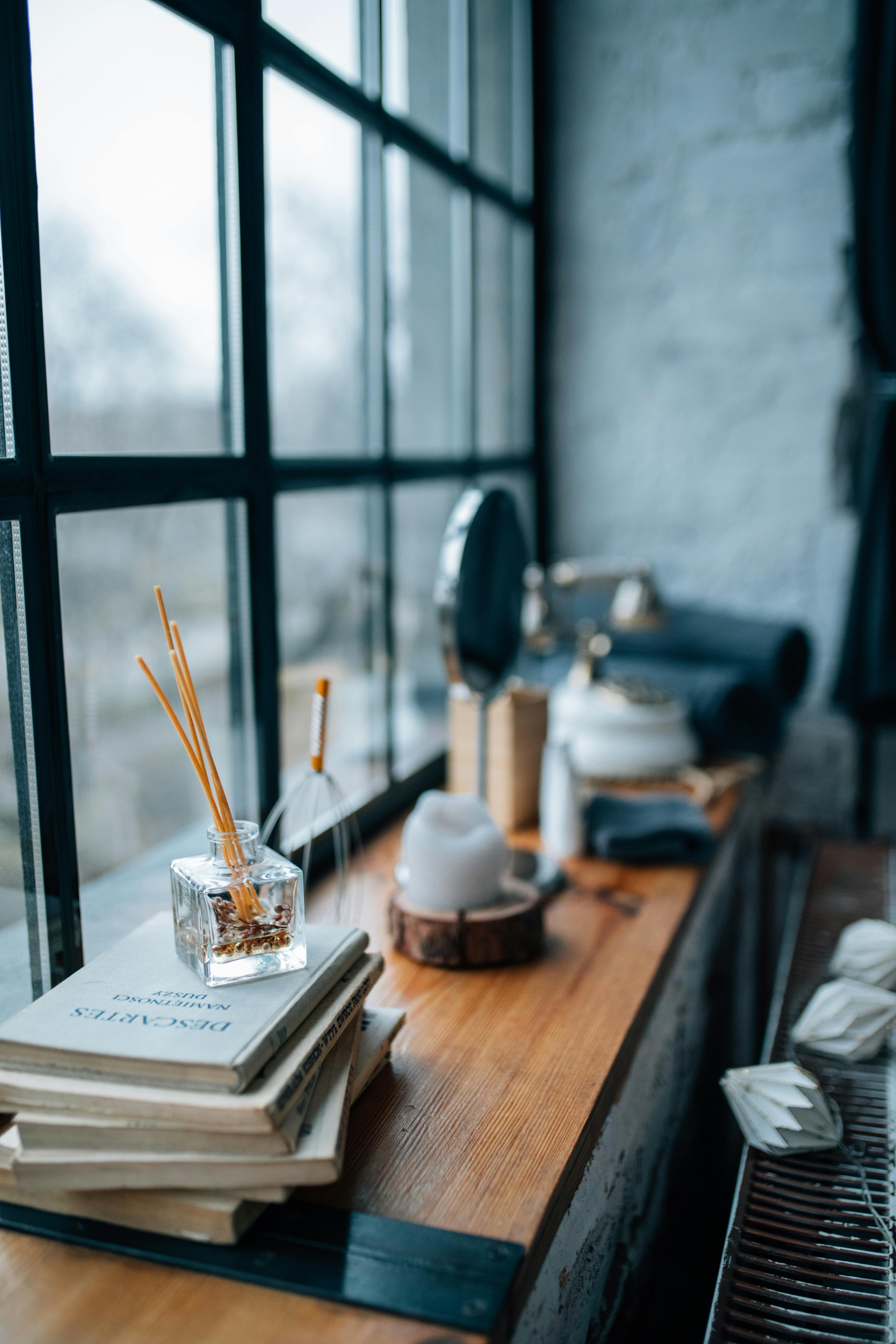 Free Aromatic reed diffuser and books create a cozy atmosphere by a glass window. Stock Photo