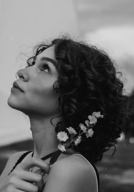 A thoughtful pose of a woman holding a delicate flower, captured in grayscale.