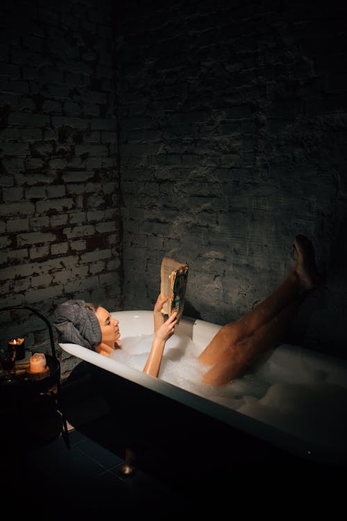 Woman Reading in Bathtub Covered with Bubbles