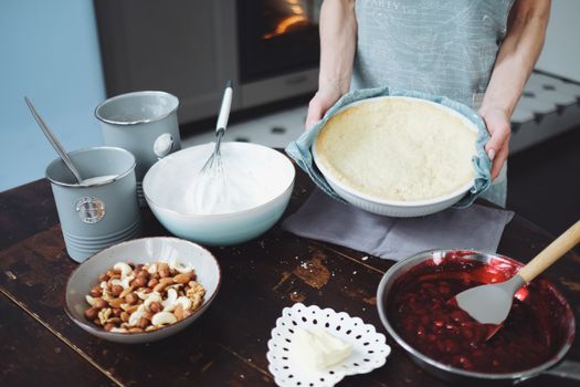 Hands preparing a homemade pie with ingredients in a cozy kitchen. Baking essentials like nuts and cherry filling are visible.