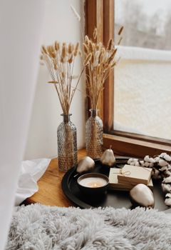 Inviting indoor scene featuring lighted candle, vases, and dried flowers by a window, perfect for a relaxing atmosphere.