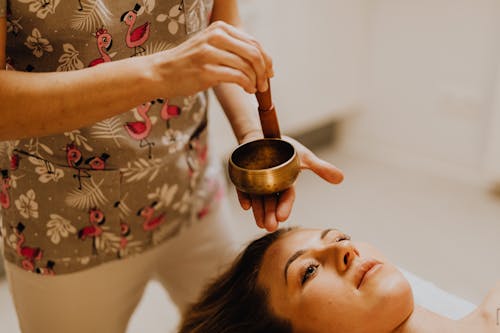 A Person Holding a Tibetan Singing Bowl Near a Woman's Face