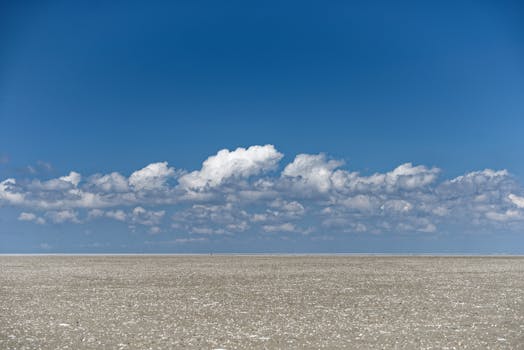 Expansive barren field beneath a cloud-filled blue sky showcasing nature's vast beauty.