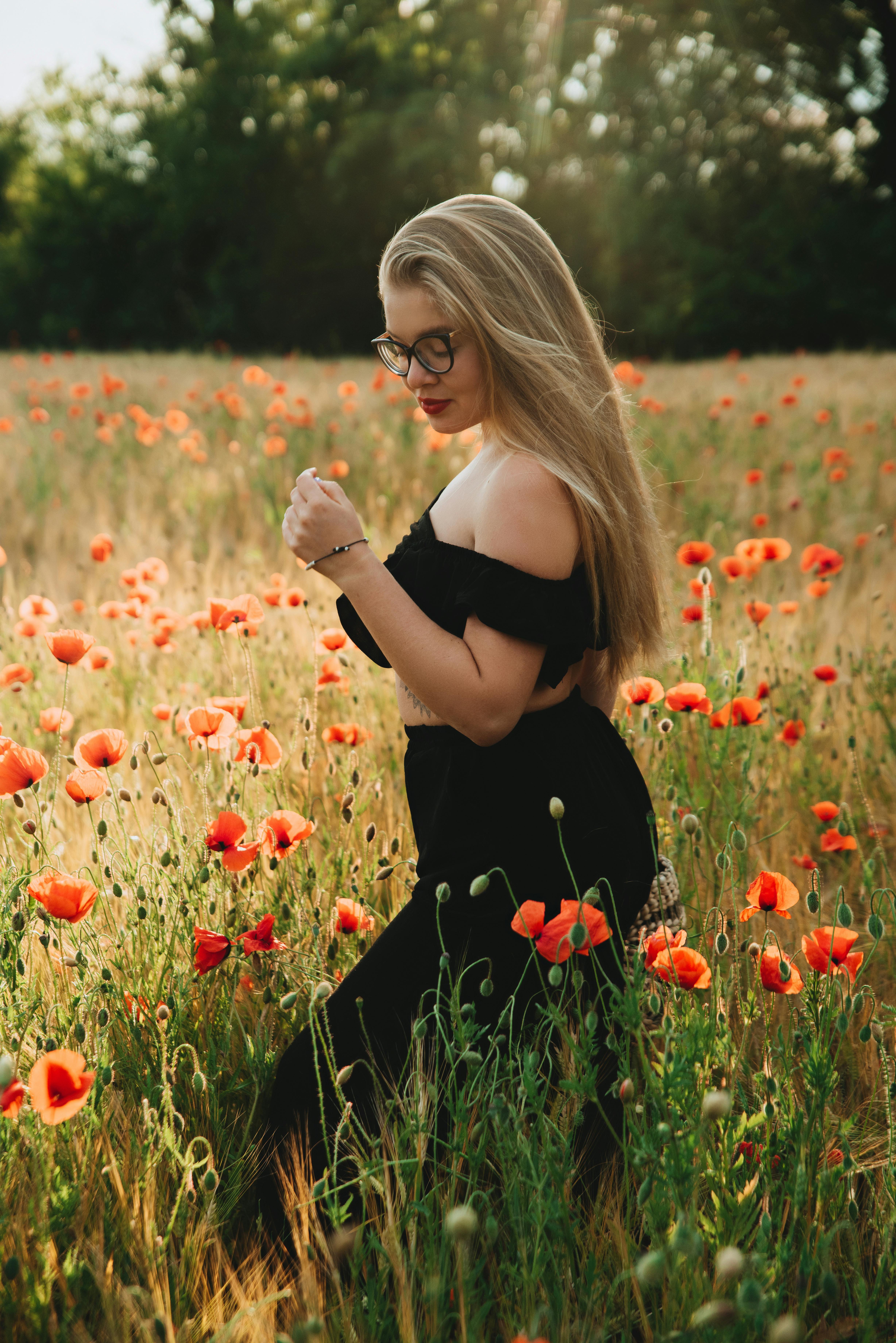 Elegant woman in a vibrant poppy field embracing nature's beauty at golden hour.