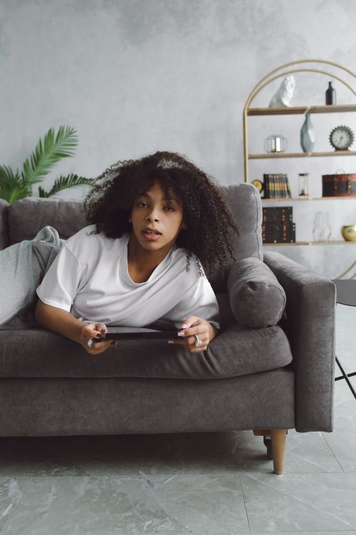 Free A relaxed woman with curly hair plays video games on a comfortable sofa indoors. Stock Photo