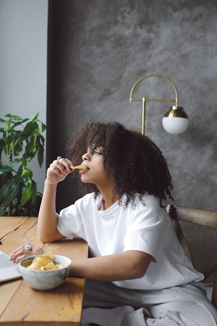 Woman Sitting On Wooden Chair Eating Potato Chips