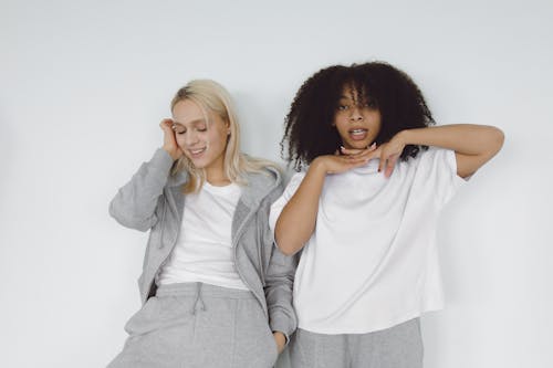 Free Two Women in White Shirt Leaning on a White Wall Stock Photo