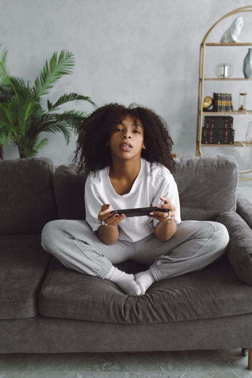 Free An African American woman playing video games while sitting on a cozy couch indoors. Stock Photo