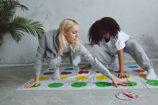 Two young women enjoying a game of Twister in a cozy indoor setting, having fun and relaxing.