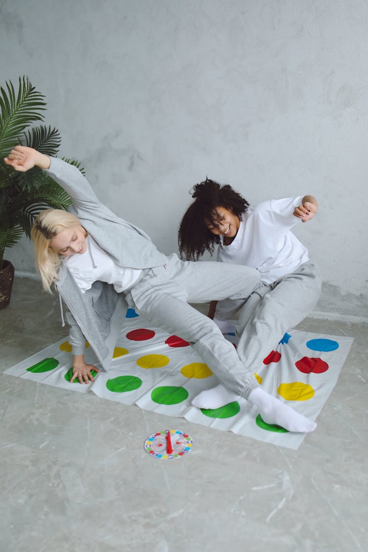 Two Women In Gray Pants And Socks Playing On A Twister Mat