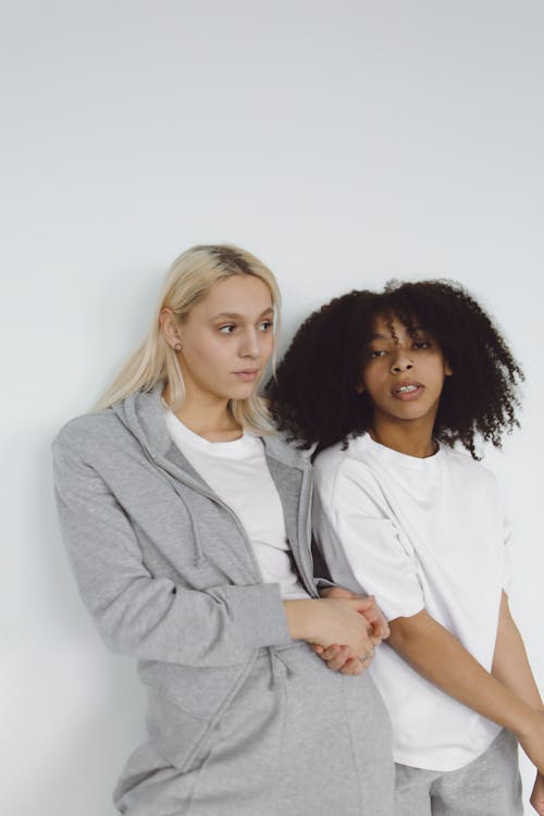 Free Two Women Wearing White Shirt Leaning on a Plain White Wall Stock Photo