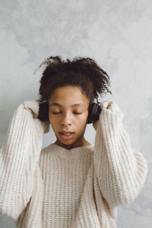 Free African American woman enjoying music with headphones in a cozy sweater. Stock Photo