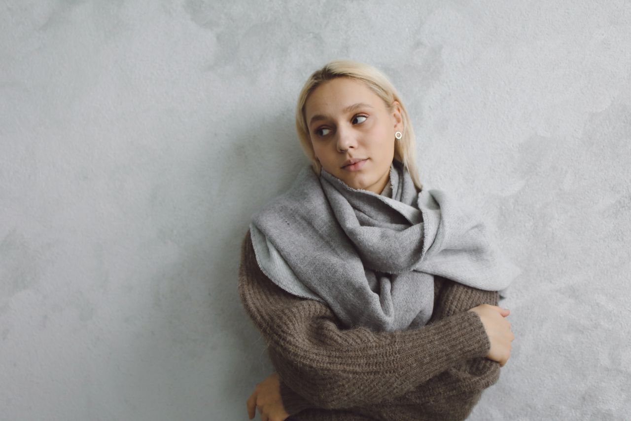 Woman in a brown sweater with a gray scarf looped at her neck