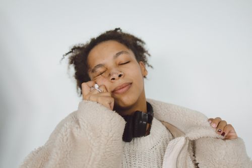 Free A serene young woman with curly hair relishes music, wearing a cozy fur coat. Stock Photo