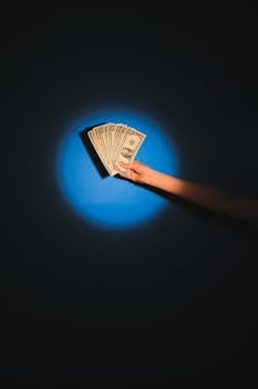 A hand holds fanned out dollar bills against a blue background, symbolizing wealth and finance.